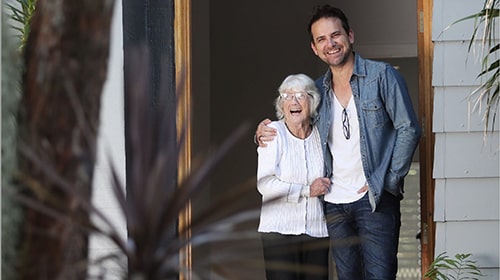 Jason stands with his arm around his mother Oma at their family home